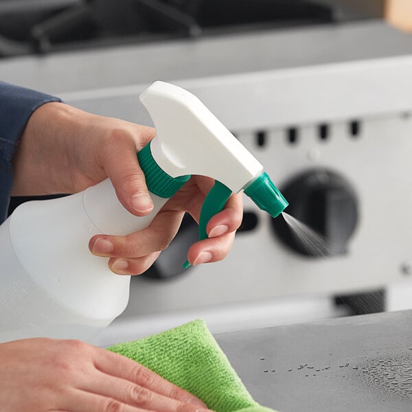 A person using a Lavex green plastic spray bottle to clean a counter.