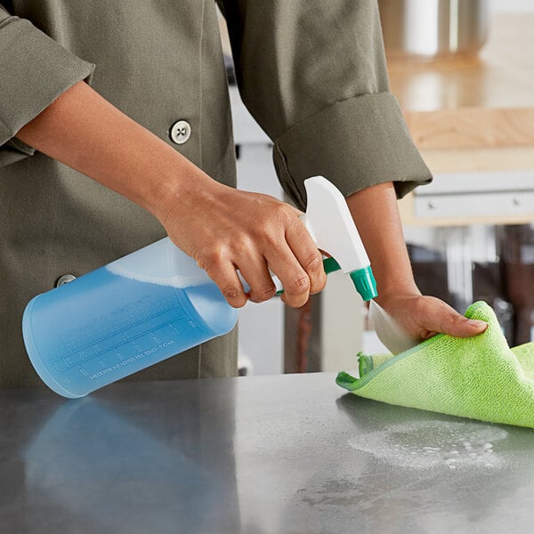 A person holding a Lavex green spray bottle and cleaning a counter with a green cloth.