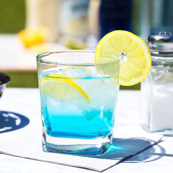 A Libbey Quartet rocks glass with blue liquid and a lemon slice.