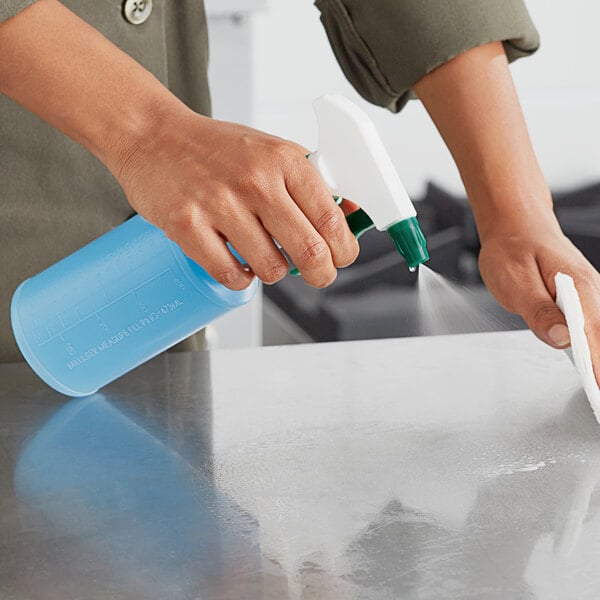 A person using a Lavex green plastic spray bottle to clean a professional kitchen counter.