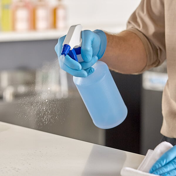 A person in blue gloves using a blue Lavex spray trigger to spray a bottle.
