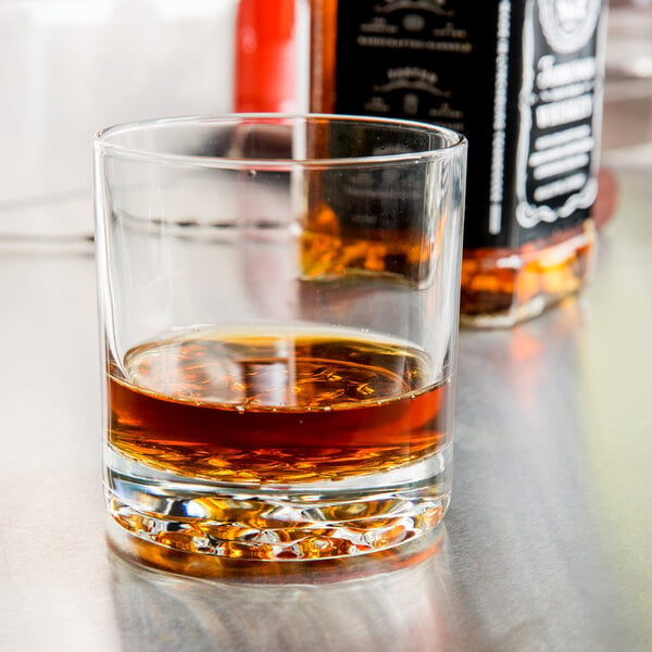 A Libbey Nob Hill Rocks glass filled with brown liquid sitting on a table in a bar.