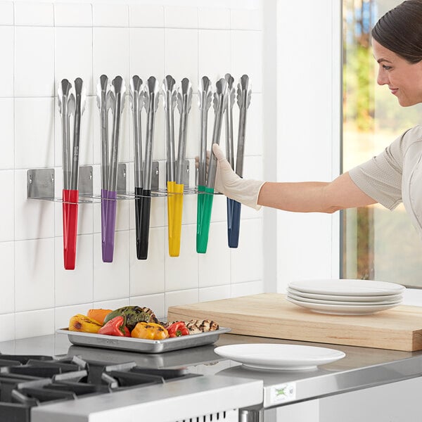 A woman wearing gloves and holding Fourt&#233; stainless steel scalloped tongs with color coated handles in a professional kitchen.