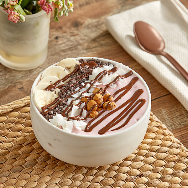 A white bowl of Vor Vegan Chocolate Hazelnut Butter with chocolate syrup and nuts on a table.