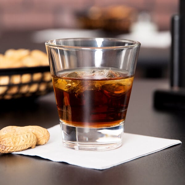 A Libbey stackable rocks glass with whiskey and ice on a table with peanuts.