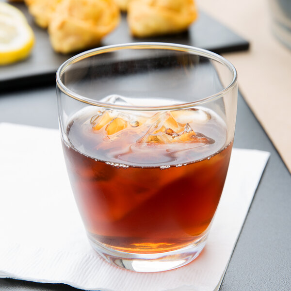 A Libbey rocks glass of brown liquid with ice and a lemon slice.