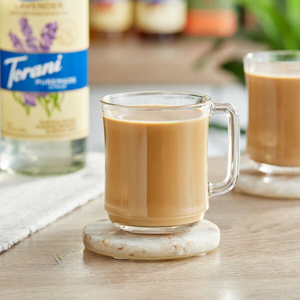 A glass mug of coffee on a marble coaster with a bottle of Torani Puremade Zero Sugar Lavender Flavoring Syrup.