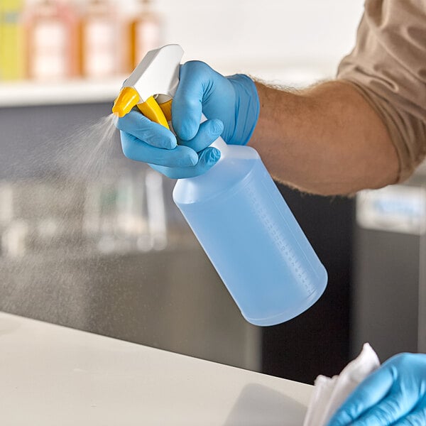 A person wearing blue gloves spraying a Lavex plastic bottle on a counter.