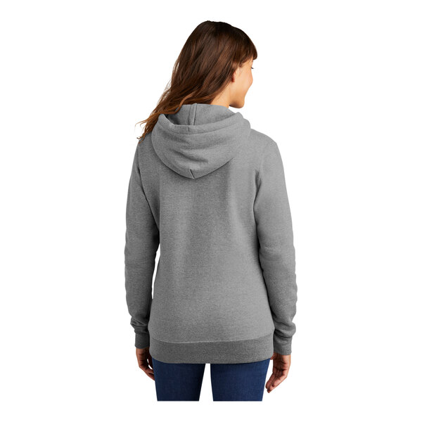 A woman wearing a Port & Company athletic heather grey pullover hoodie.