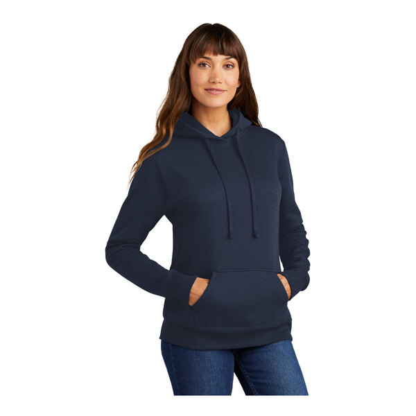 A woman wearing a Port & Company navy blue pullover hoodie.