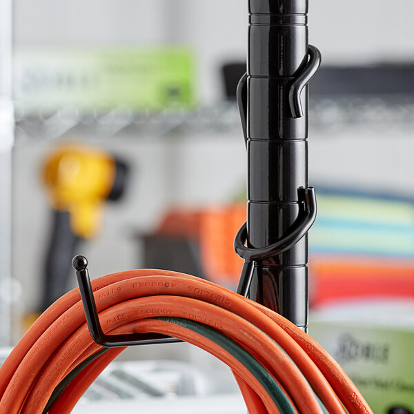 A black metal utility hanger with a coiled orange and green hose.