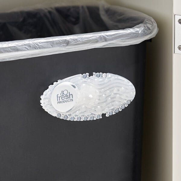 A black Fresh Products Curve air freshener holder on a trash can with a plastic bag and a white shoe on the side.