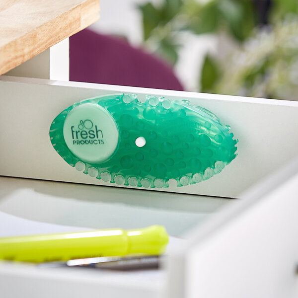 A green Fresh Products Curve air freshener with a white holder on a white surface.