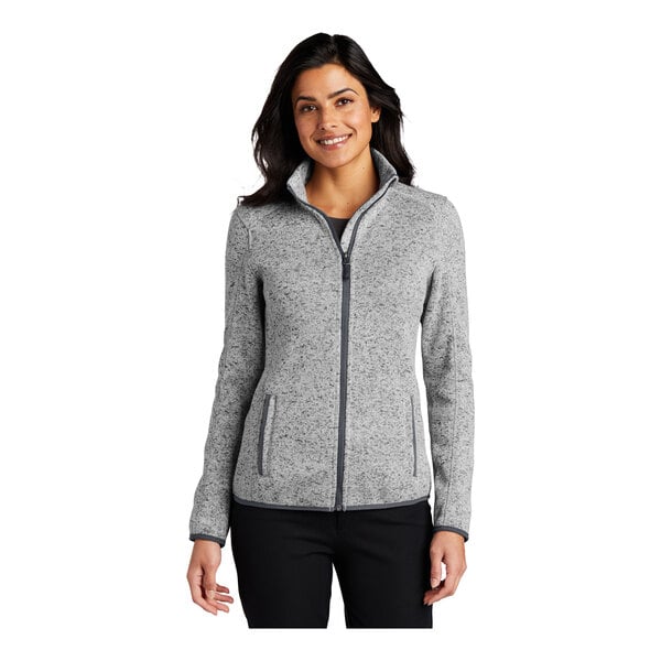 A woman wearing a gray Port Authority fleece sweater jacket with a full-zip.