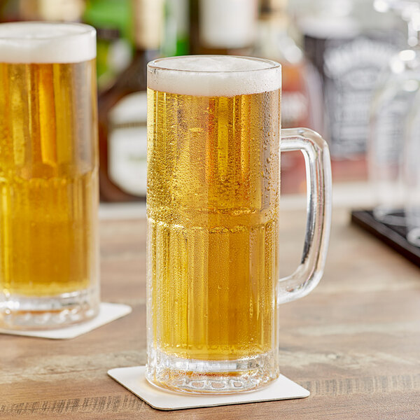 Two Acopa tall beer mugs filled with beer on a wooden table.