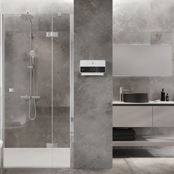 A close up of an Ariston tankless water heater installed in a modern bathroom with a shower and sink.