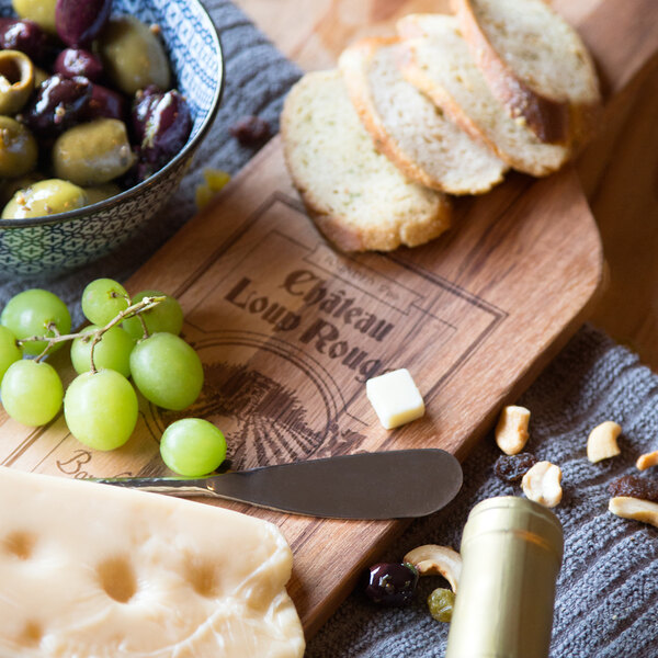 An Ironwood acacia wood paddle board with cheese, grapes, and olives on it next to a bottle of wine.