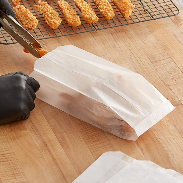 A person using tongs to hold fried shrimp in a Kari-Out glassine bag.