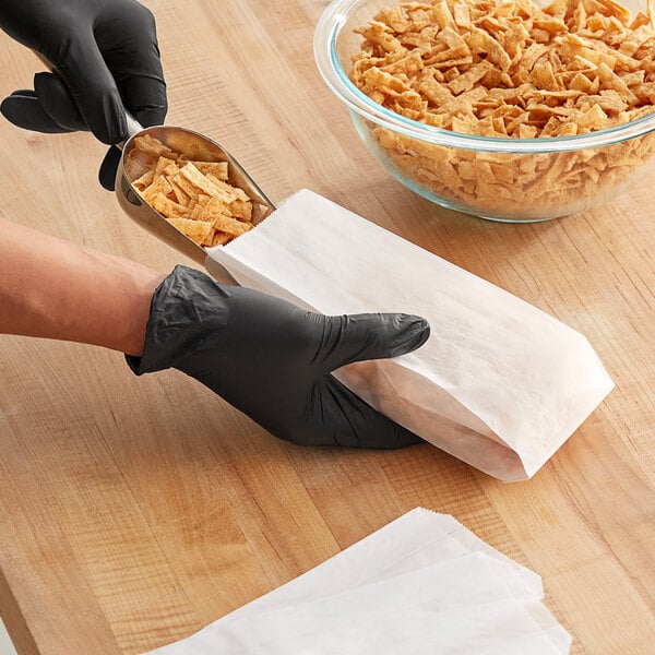 A person in black gloves putting a Kari-Out Company glassine bag of cereal into a bowl.