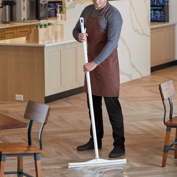 A man in an apron using a Vikan white rubber floor squeegee with a white handle to clean a floor.