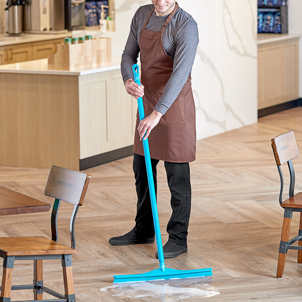 A man in an apron using a Vikan blue rubber floor squeegee to clean a floor.