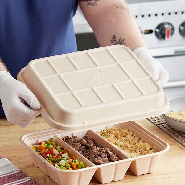 A man in a white shirt holding a World Centric compostable fiber catering pan with food in it.