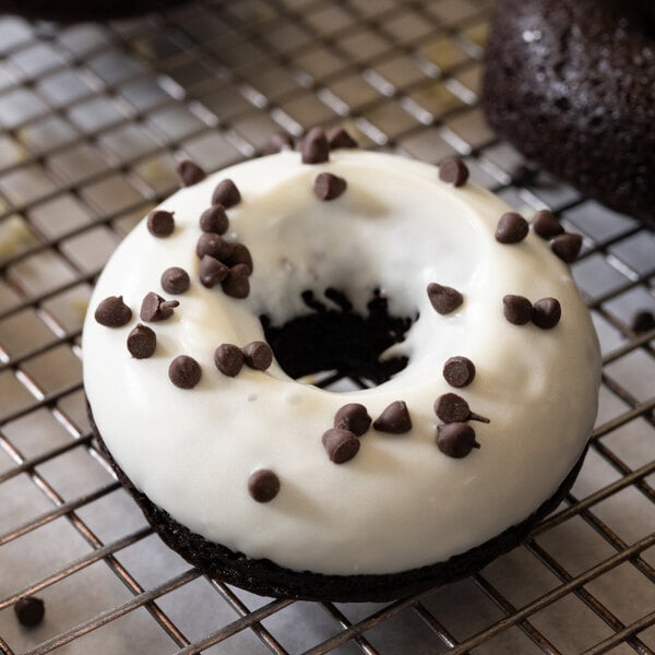 A donut with Ghirardelli white coating and chocolate chips on a cooling rack.