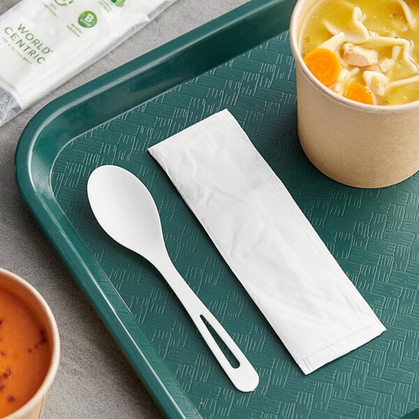 A green tray with a bowl of soup and a white World Centric compostable spoon with a napkin.