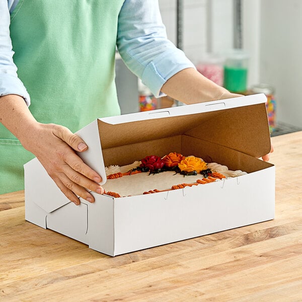 A person is putting a cake into a white Southern Champion bakery box.