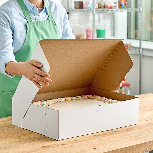 A woman opening a white Southern Champion bakery box to reveal a cake.