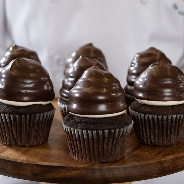 A chef holding a wood tray of chocolate cupcakes with Ghirardelli Dark Coating on top.