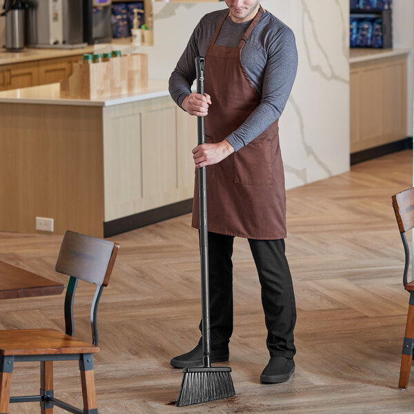 A man in an apron sweeping the floor with a Vikan angled broom.