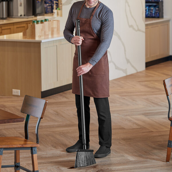 A man holding a Vikan black angled broom head on a pole sweeping the floor in a restaurant.