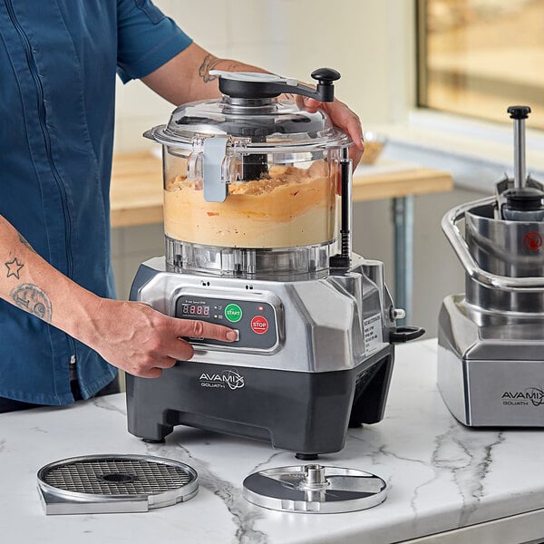 A commercial food processor with a clear plastic bowl and digital controls, shown in use on a kitchen counter.