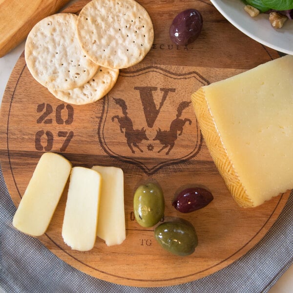 An Ironwood acacia wood round serving board with a 2007 wine barrel engraving holding cheese and crackers.
