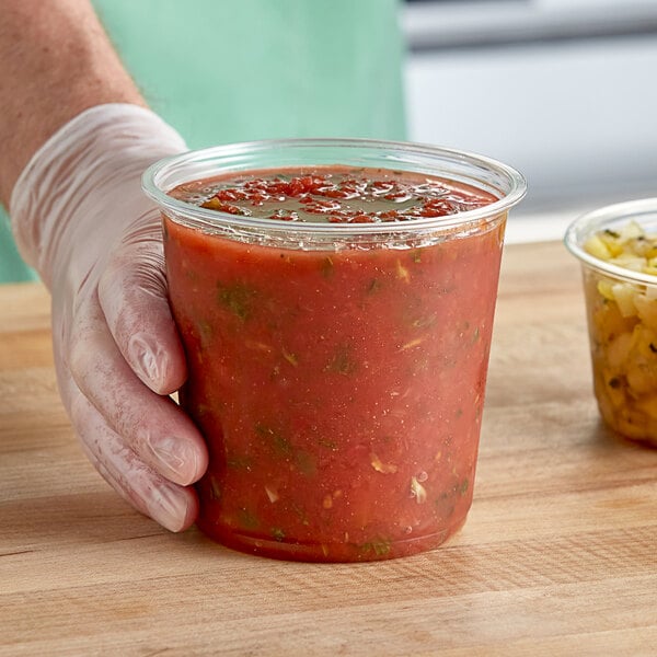 A hand holding a Choice clear plastic deli container of tomato sauce.