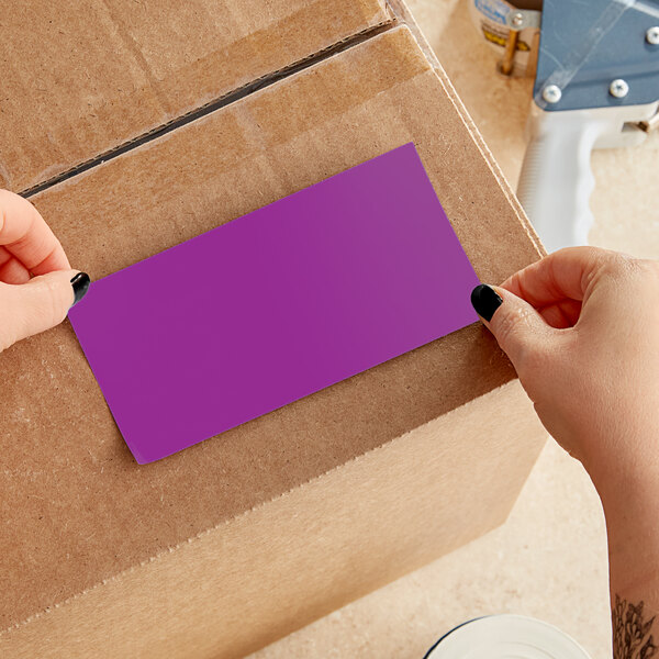 A person using a white and blue tool to cut a purple rectangular Lavex label from a roll.