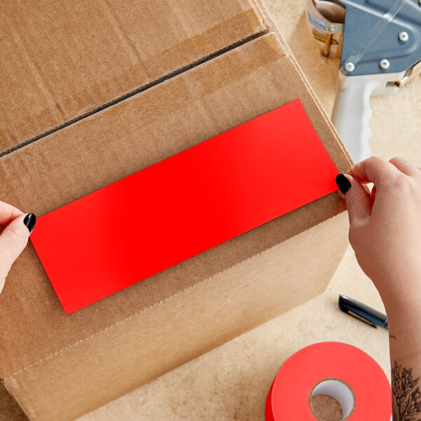 A person's hands cutting a red rectangular Lavex inventory label from a roll.