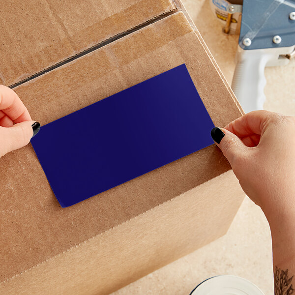 A person's hands cutting a blue rectangular label from a cardboard box.