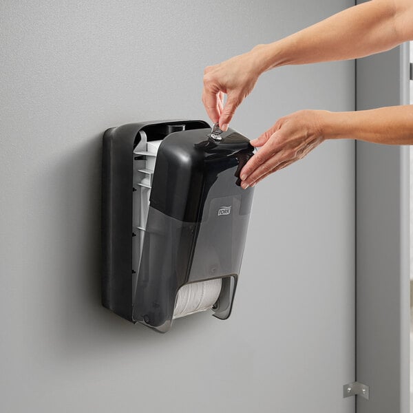 A person installing a black Tork double roll toilet paper dispenser.