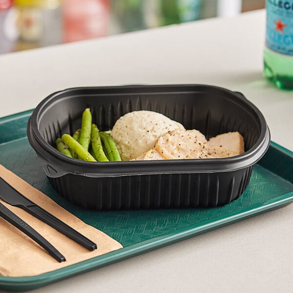 A black Pactiv MealMaster container with food on a tray with a black knife and fork.