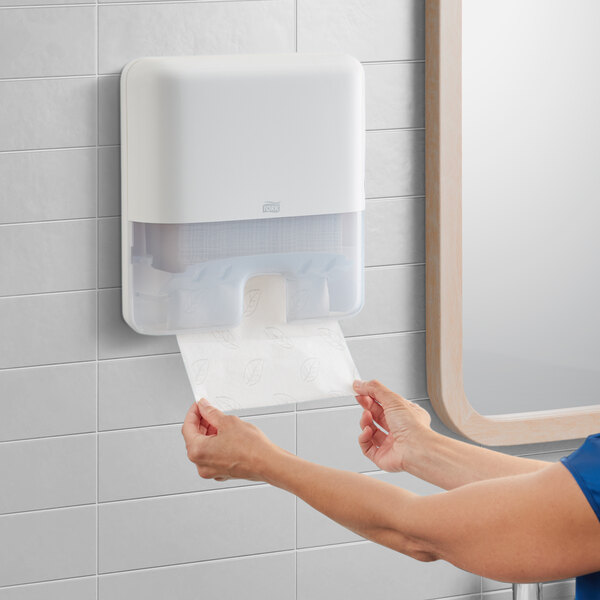 A woman using a Tork white mini wall-mount multifold hand towel dispenser.