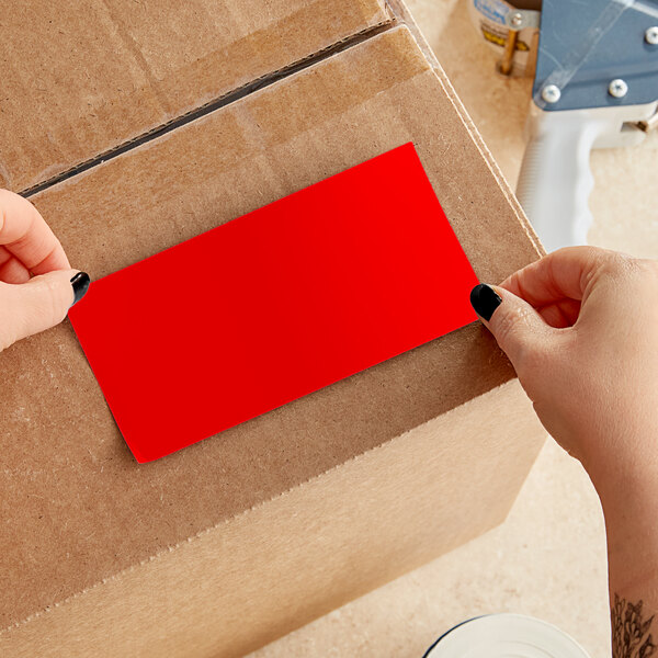 A person's hands using a red rectangular Lavex inventory label.