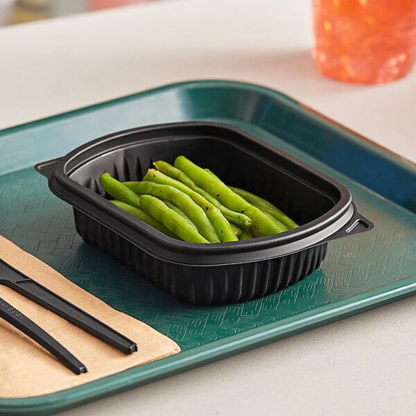 A Pactiv black rectangle container filled with green beans on a table.