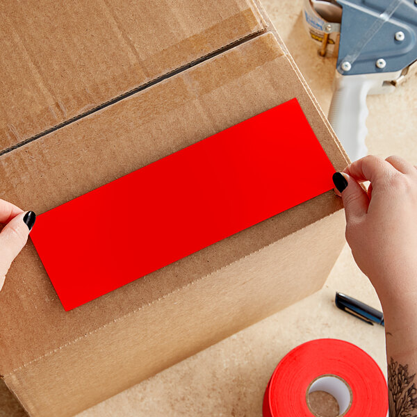 A person's hands cutting a red rectangular paper label from a roll.