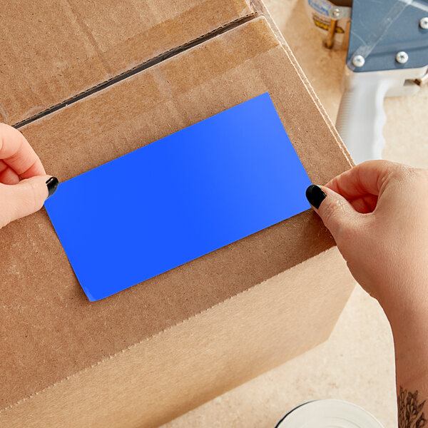 A person's hands cutting a light blue rectangular piece of paper from a box.