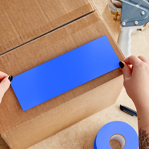 A person's hands cutting a light blue rectangular piece of paper.