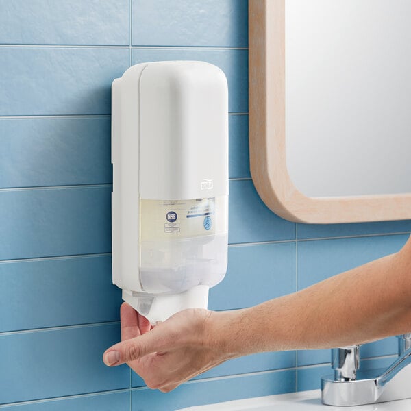 A person using a Tork manual hand sanitizer dispenser.