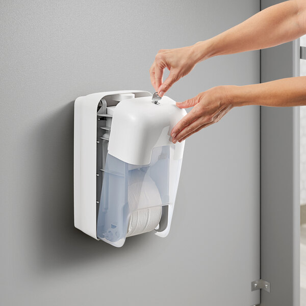 A person's hands putting toilet paper rolls into a white Tork OptiServe dispenser.