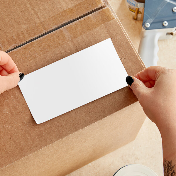A person using two hands to apply a white rectangular Lavex label to a cardboard box.